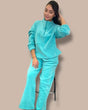 Person wearing an aqua tracksuit sitting on a stool against a beige background
