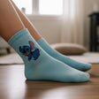Kids pale aqua crew socks with a running blue Stitch print on the side, worn on crossed feet