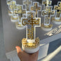 Small white cross topper with gold Arabic lettering set in a flower filled pot