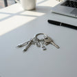 Architect keychain with compass, protractor, brush, and house charms on a desk