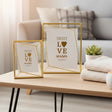 Two gold frames with faceted geometric cages on an oak table with hairpin legs