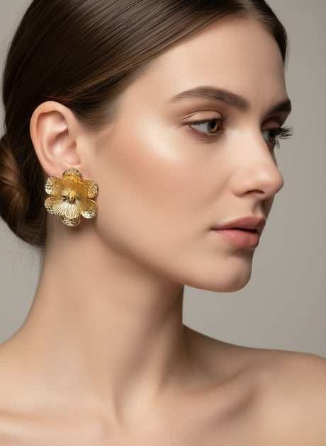 Woman wearing gold floral earrings against a neutral background