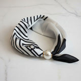 Black and white patterned foulard with a pearl accent on a marble surface