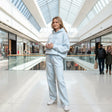 Woman in a light blue jogging set holding a coffee cup in a shopping mall