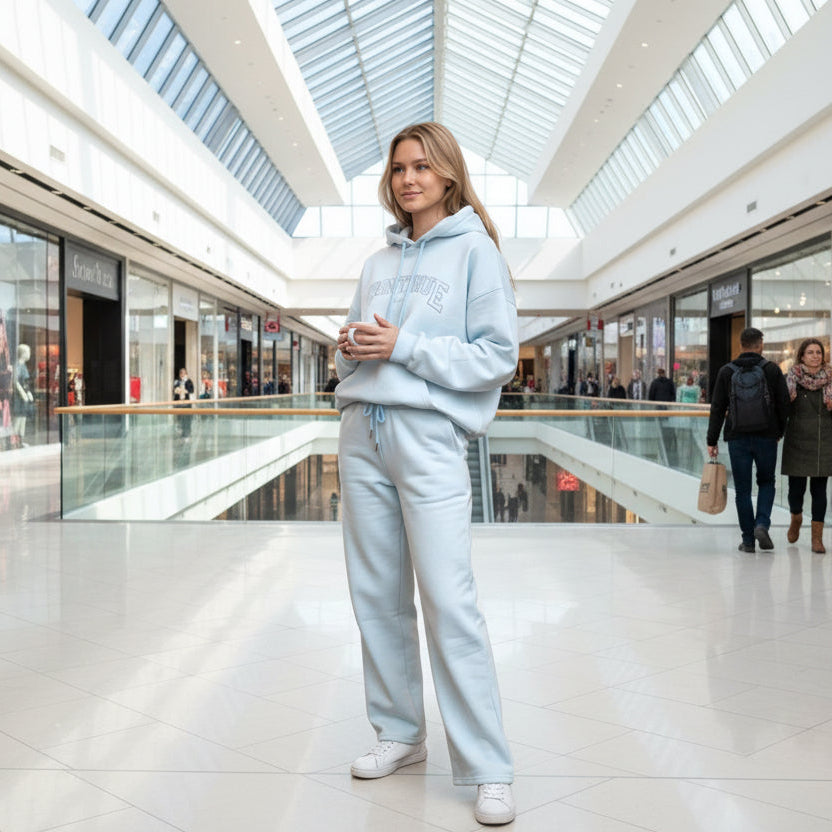 Woman in a light blue jogging set holding a coffee cup in a shopping mall