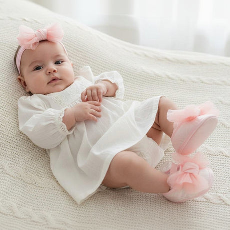 Newborn on a knit blanket in a pale pink tulle bow headband with ruffled pink tulle soft soled booties