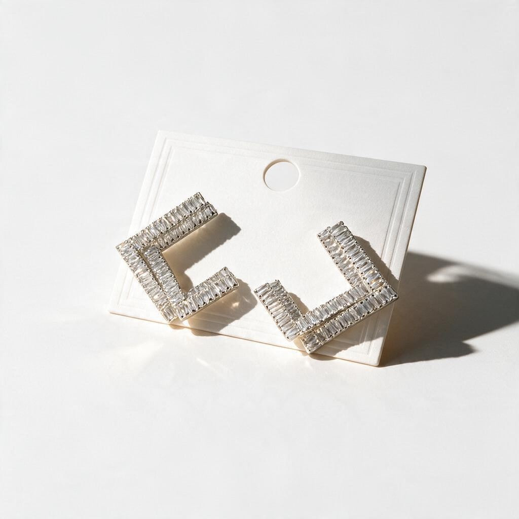 Silver tone open square earrings set with clear baguette crystals on a white card