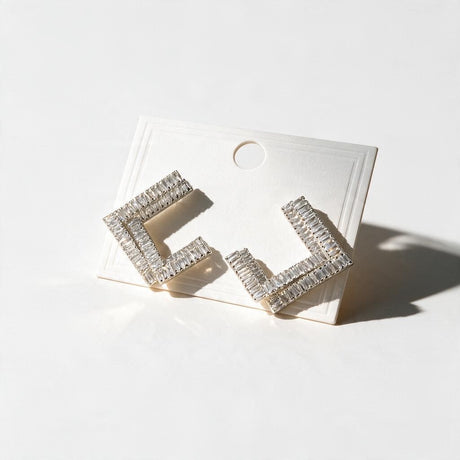Silver tone open square earrings set with clear baguette crystals on a white card