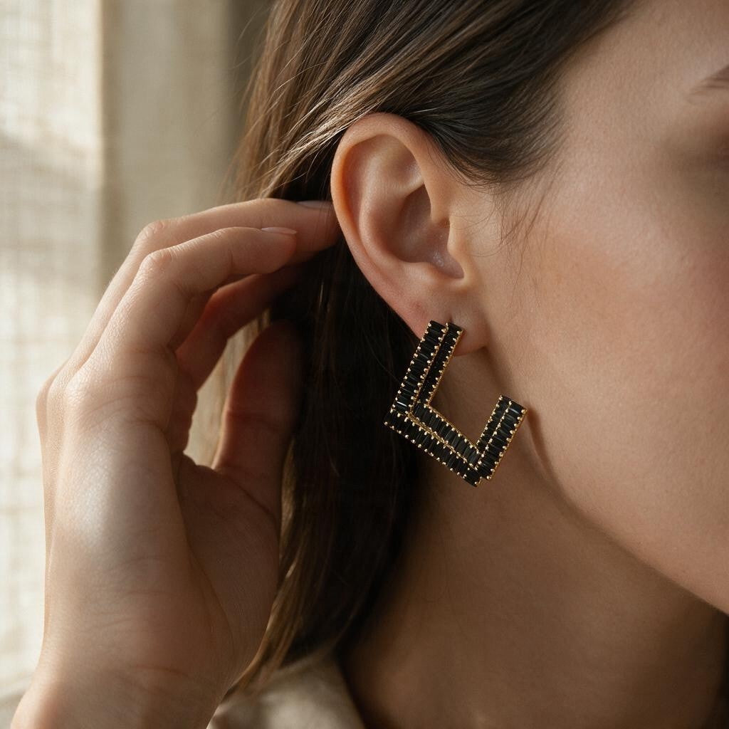 Woman wearing a black baguette crystal open square earring with a gold tone frame