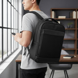 Person wearing a black backpack in an indoor setting with a desk and bookshelf