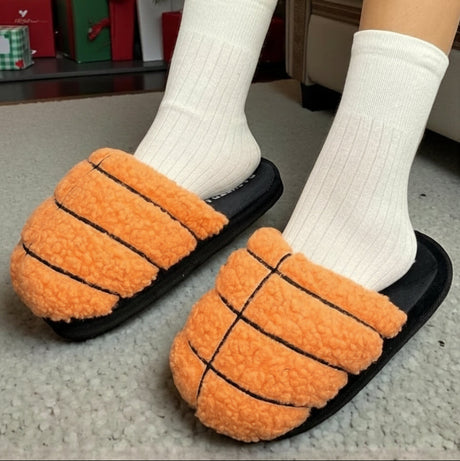 Orange basketball slippers with black lines worn with white socks on a carpeted floor