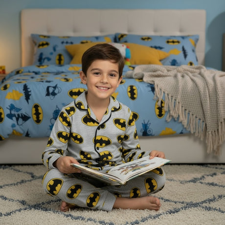 Child in Batman pajamas reading a book in a bedroom with matching bedding