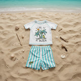 A children's two-piece beach outfit, featuring a white short-sleeve rash guard with a palm tree graphic, paired with mint-and-white striped shorts