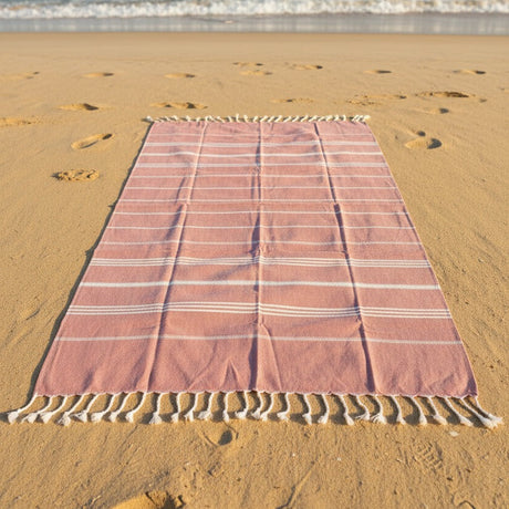 Oversized pink striped beach towel with decorative fringe edges on sandy surface