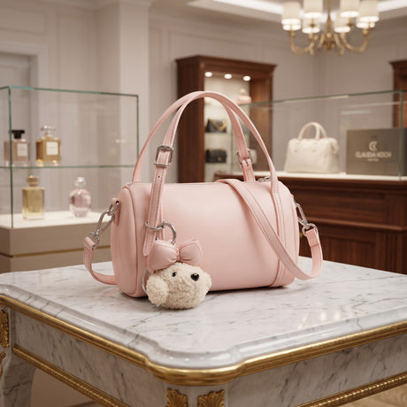Pink barrel crossbody bag with a bear charm on a marble table