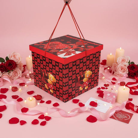 Red heart print gift box with a rope handle on a pink table