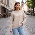 Woman in a beige brushed wool crew neck sweater and light jeans with a gold pendant necklace on a cobbled street
