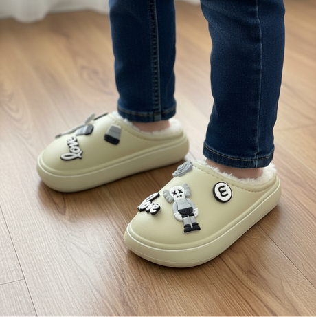 Child in jeans wearing beige fur lined clog slippers with toe charms on a wooden floor