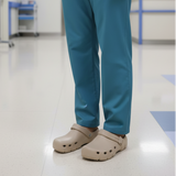 Person wearing blue scrubs and beige clogs on a hospital floor