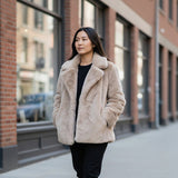 Woman wearing a beige fur coat walking on a city street