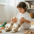 Kids beige knee high socks with a small dinosaur motif and a brown stripe cuff