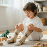 Kids beige knee high socks with a small dinosaur motif and a brown stripe cuff