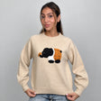 Beige knit sweater with a fuzzy elephant patch, holding the ribbed hem