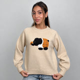 Beige knit sweater with a fuzzy elephant patch, holding the ribbed hem