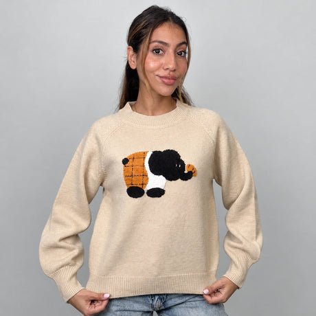 Beige knit sweater with a fuzzy elephant patch, holding the ribbed hem