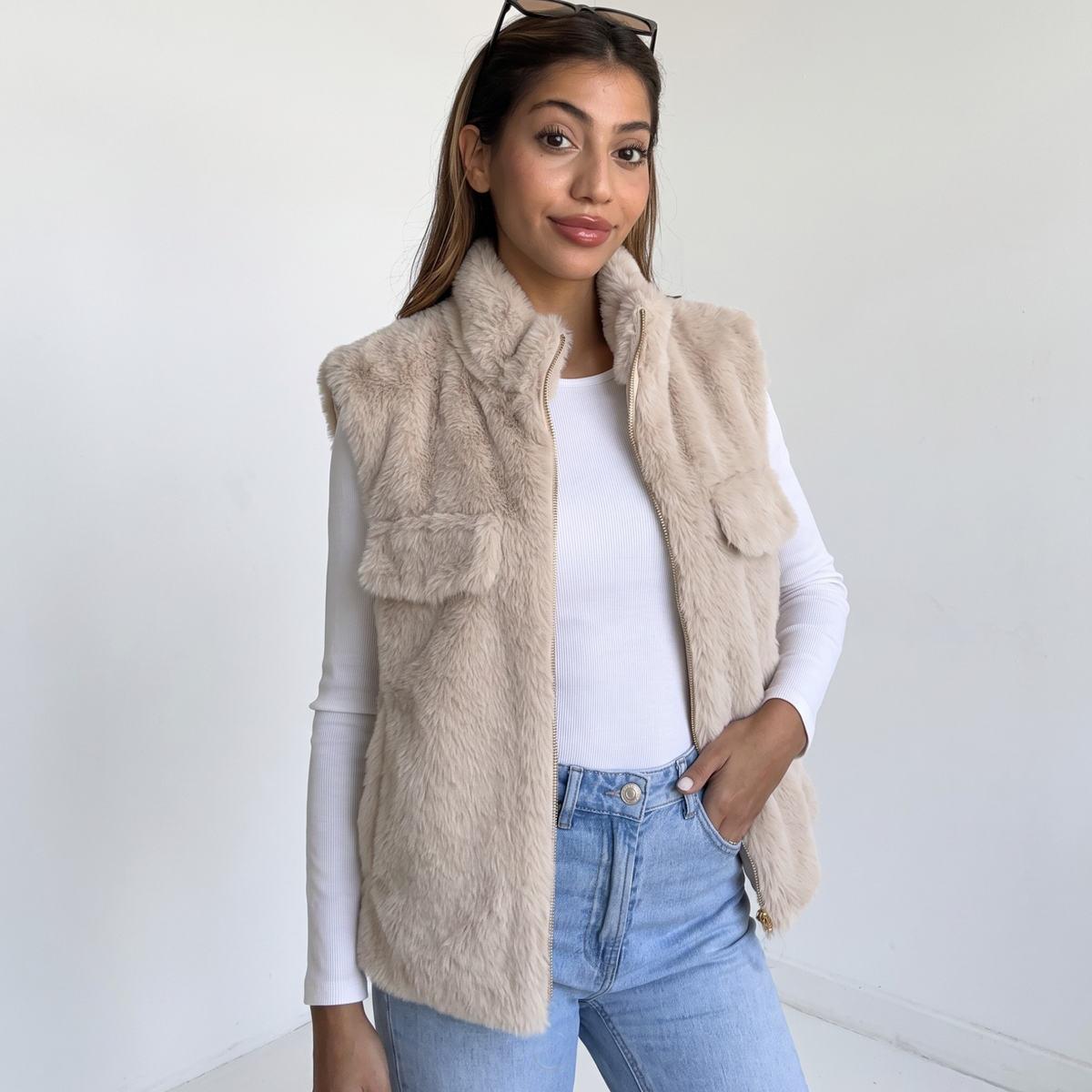 Beige faux fur sleeveless gilet with stand collar and gold zip over a white long sleeve top