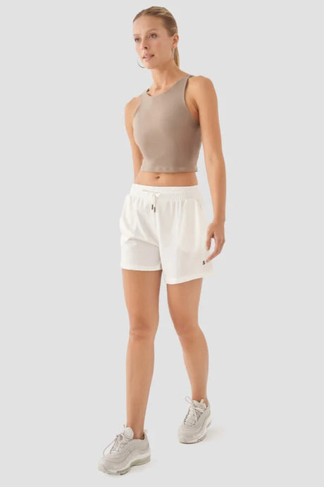 Woman wearing a beige tank top and white shorts on a light grey background
