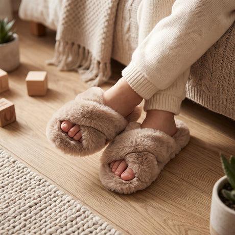 Child wearing beige fluffy crossover slippers beside a bed with wooden blocks nearby