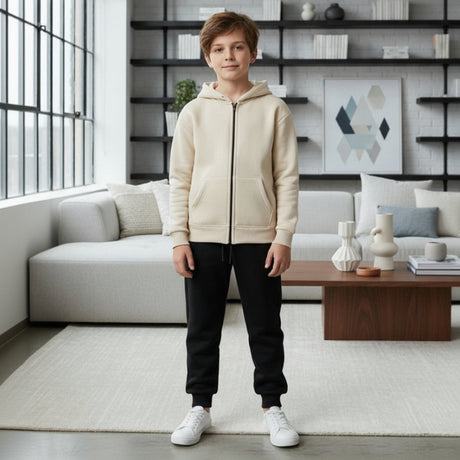 Boy in a cream beige zip up hooded jacket paired with black joggers and white trainers
