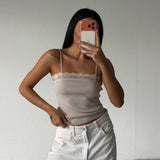 Person wearing a beige top and white pants taking a mirror selfie against a plain white wall