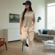 Woman in beige outfit and black cap standing in a living room