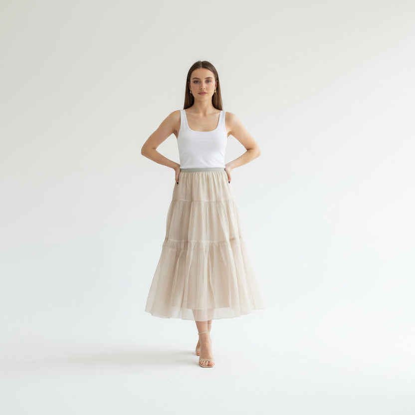 Woman wearing a white tank top and beige tiered skirt on a white background