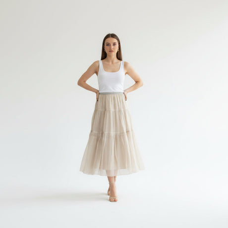 Woman wearing a white tank top and beige tiered skirt on a white background