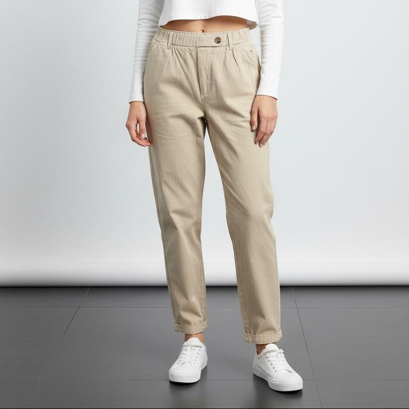 Woman wearing a white long-sleeve top and beige pants on a plain background
