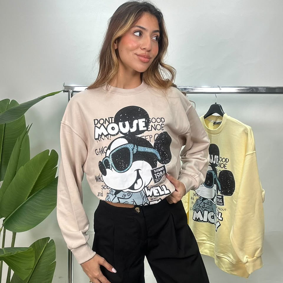 Beige rhinestone graphic sweatshirt worn with black pants beside a clothing rail