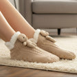 Beige slippers with teddy bear design worn indoors on a carpeted floor.