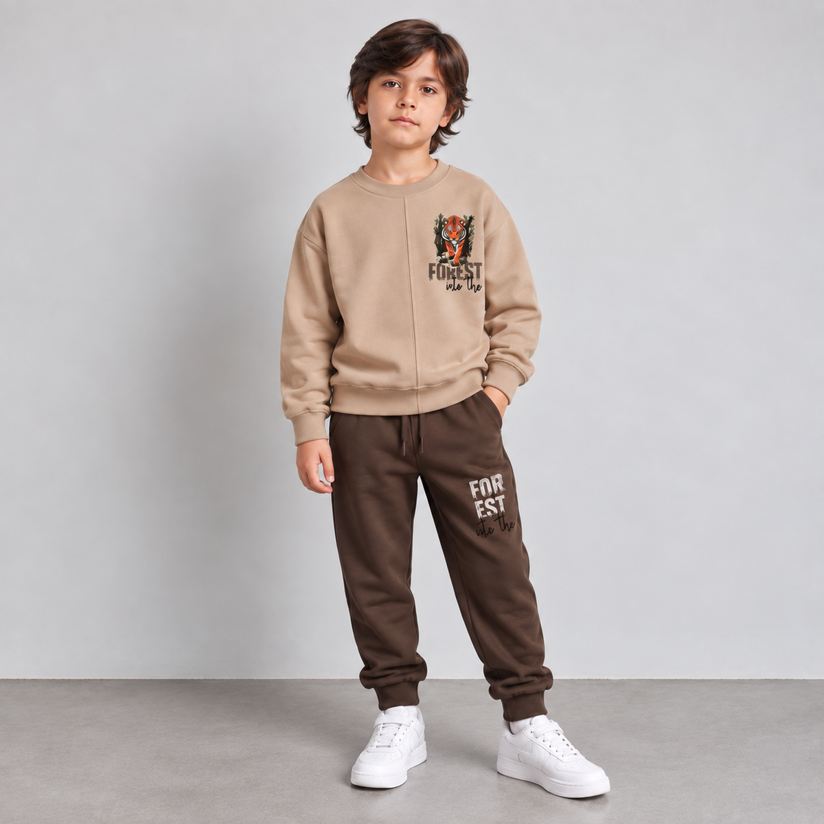 Boy standing in a beige tiger forest sweatshirt and brown joggers, front view