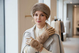 Woman wearing a fur hat, scarf, and beige leather gloves in a store setting