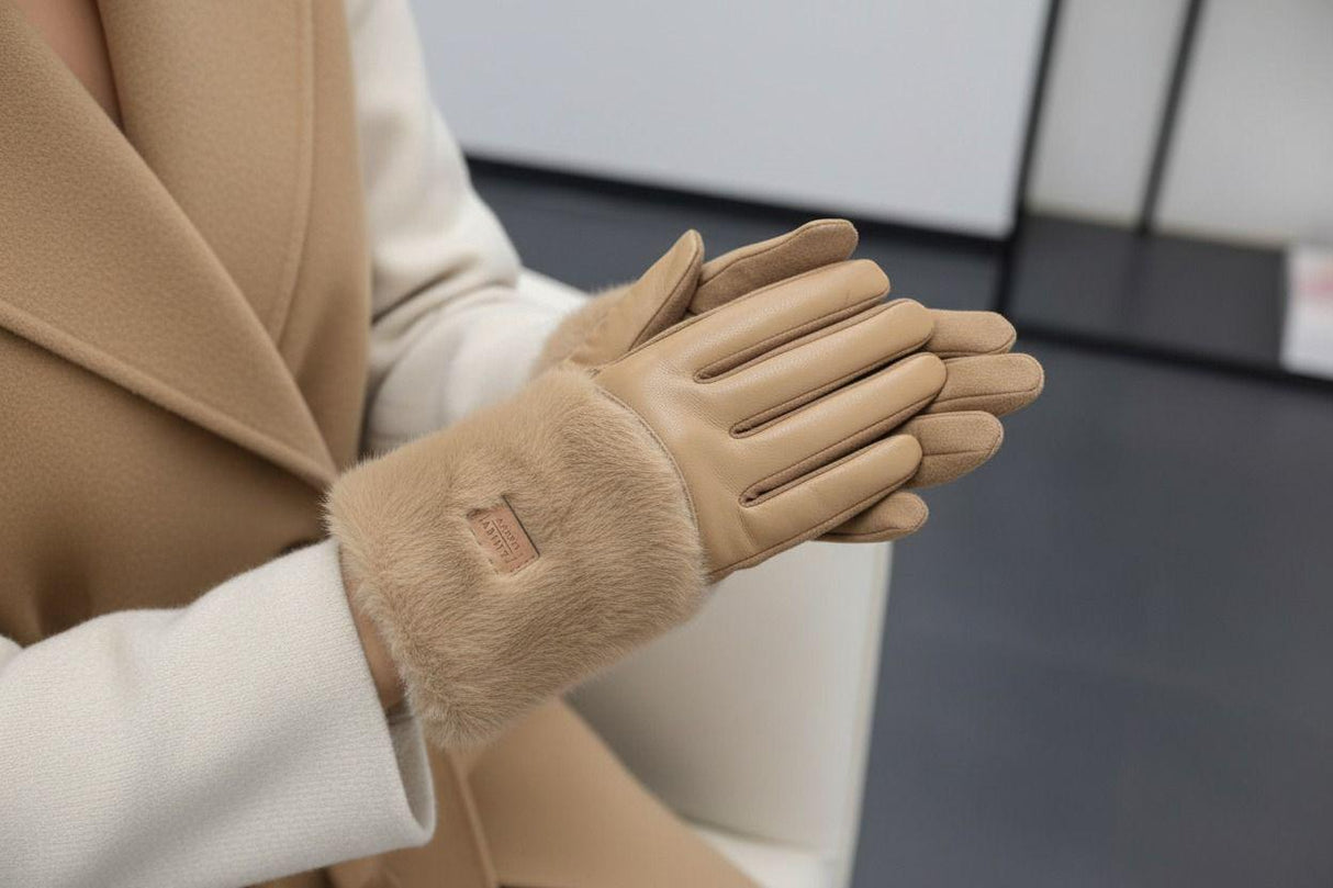 Beige leather gloves with fur cuff worn by a person in a beige coat against a blurred indoor background
