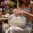 Woman with a beige woven straw clutch bag sitting in an outdoor cafe setting