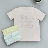 Pink script tee laid flat with folded yellow and blue tees beside it