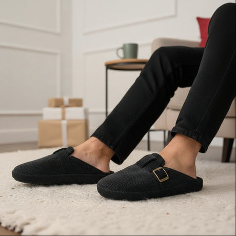 Person wearing black slippers with a belt buckle in a home setting