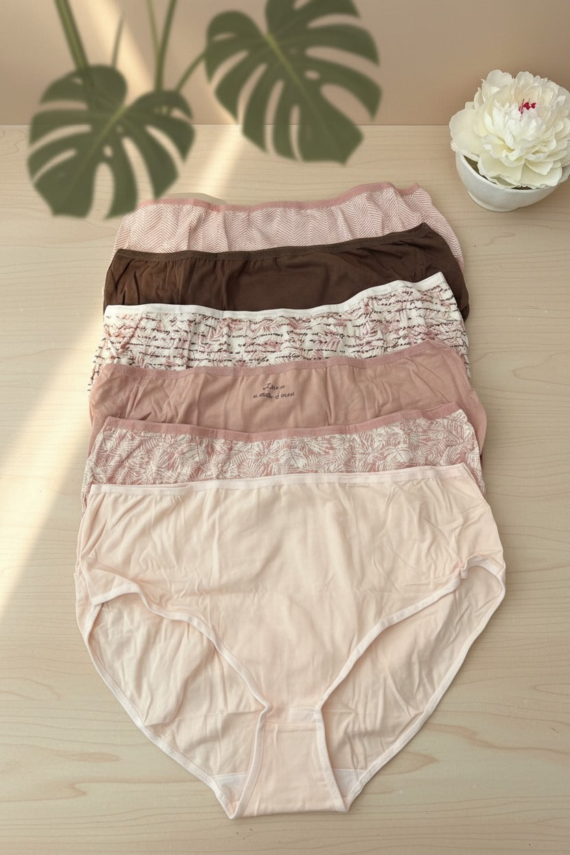 Pale pink, cocoa and floral briefs spread on a wooden table under palm leaf shadows