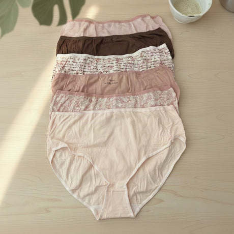 Pale pink, cocoa and floral briefs spread on a wooden table under palm leaf shadows