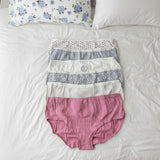 Full coverage briefs stacked on a white bed, a solid pink pair on top