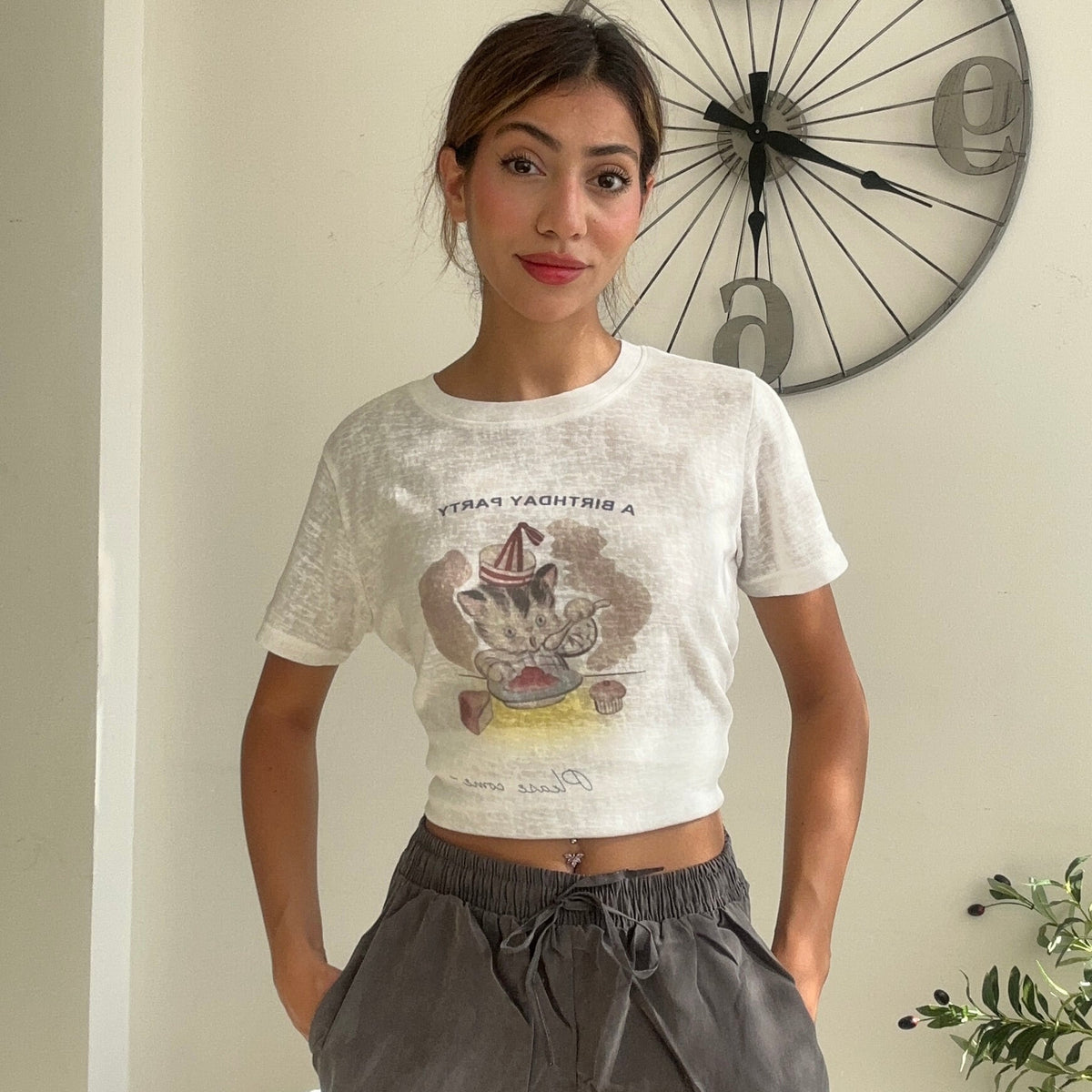 Cream crop tee with a party kitten illustration, worn with grey wide leg trousers